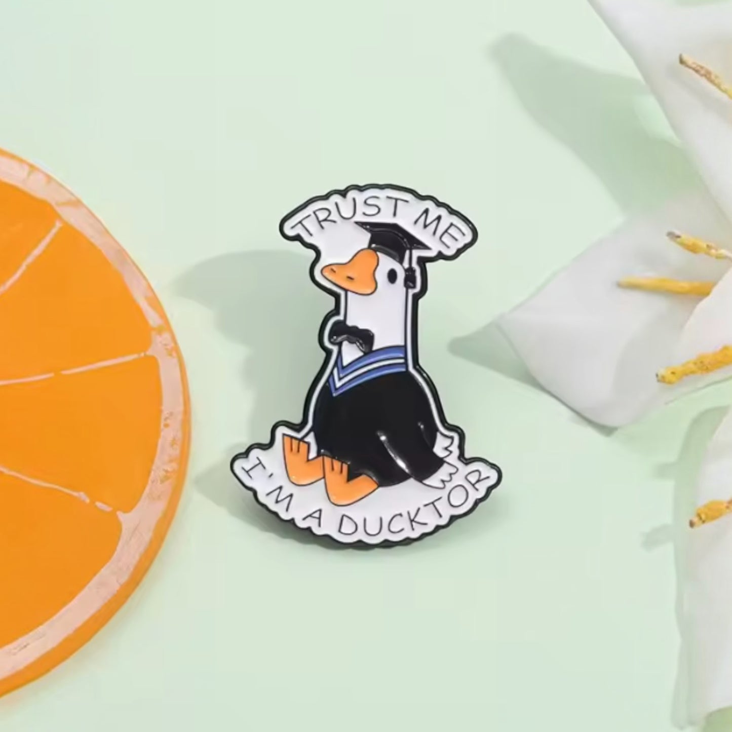 Pins & Co. enamel lapel pin featuring a duck in a graduation cap and gown with the text Trust Me I'm a Ducktor