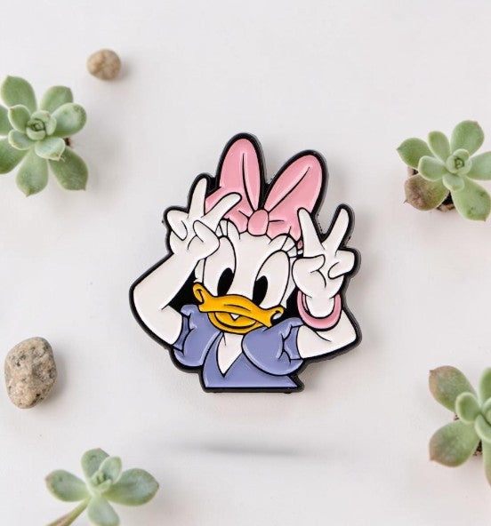 Pins & Co. Daisy Duck enamel lapel pin featuring the character making a peace sign with a pink bow and purple dress.