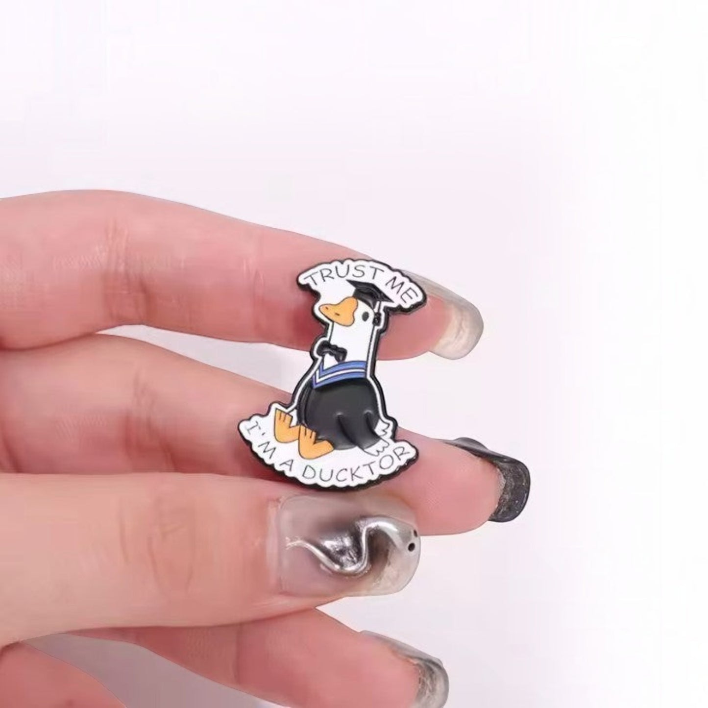 Pins & Co. enamel lapel pin featuring a duck in a graduation cap and gown with the text Trust Me I'm a Ducktor