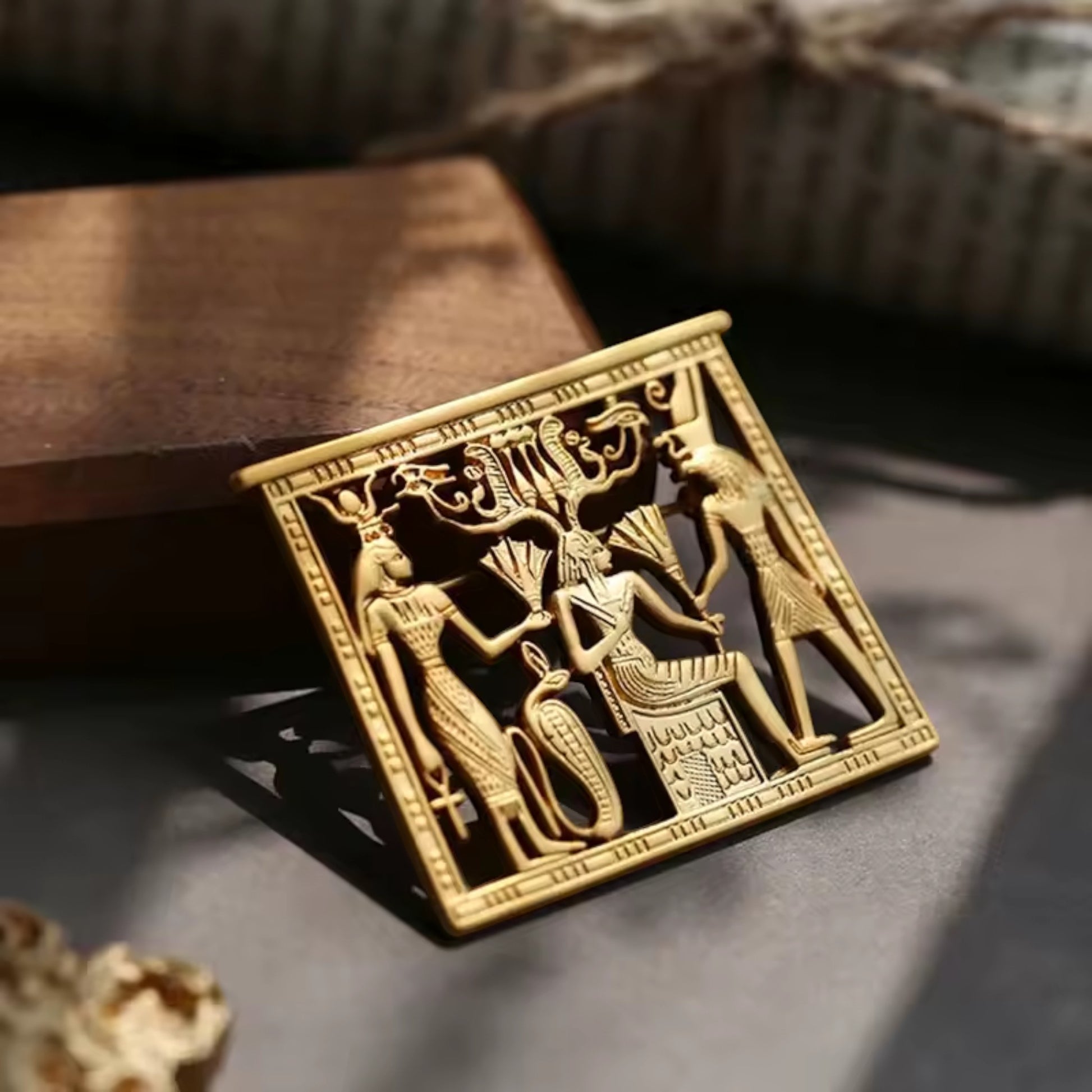 Pins & Co. gold metal Egyptian relief plaque with intricate deity engravings on a wooden base for home decor.