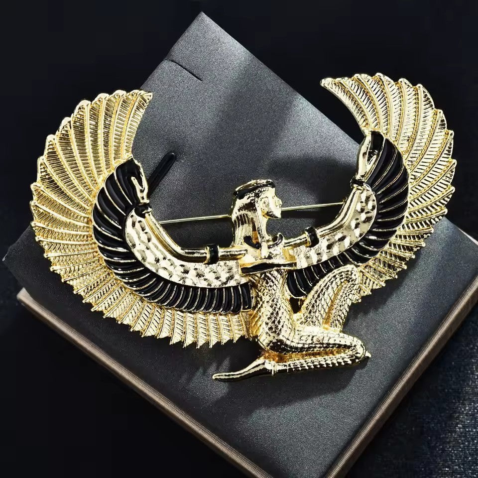 Pins & Co. gold-tone Egyptian winged goddess brooch with black enamel accents on a display box.