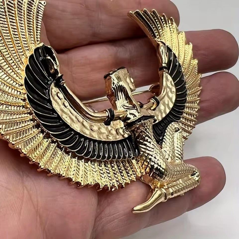 Pins & Co. gold-tone Egyptian winged goddess brooch with black enamel detailing held in a hand.