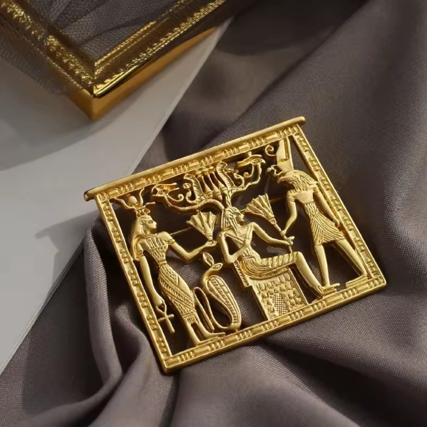 Pins & Co. gold Egyptian relief plaque featuring intricate deity engravings on a grey fabric background